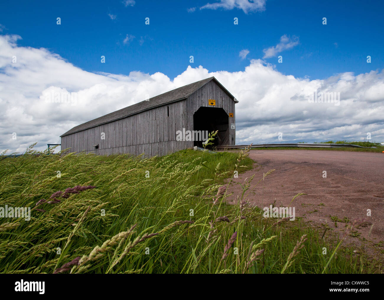 New Brunswick covered bridge on a rural road across the Tantramar Marsh under a blue, cloudy summer sky. Stock Photo