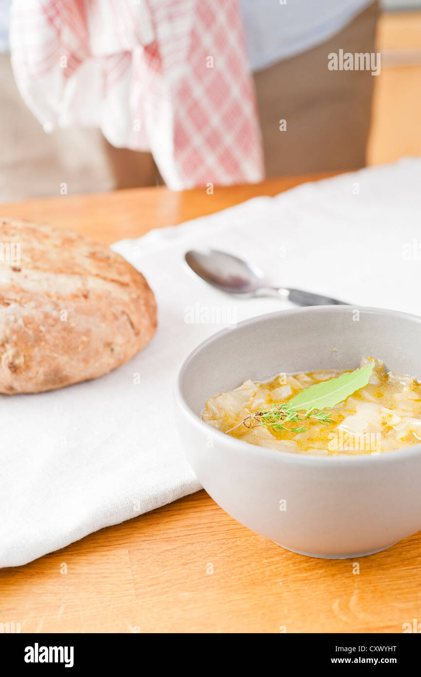 Hot onion soup and freshly baked bread on wooden counter in a kitchen with the chef in the background. Stock Photo