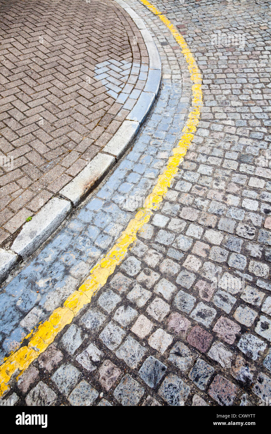 Yellow line road markings on cobbled street corner kerb, UK Stock Photo