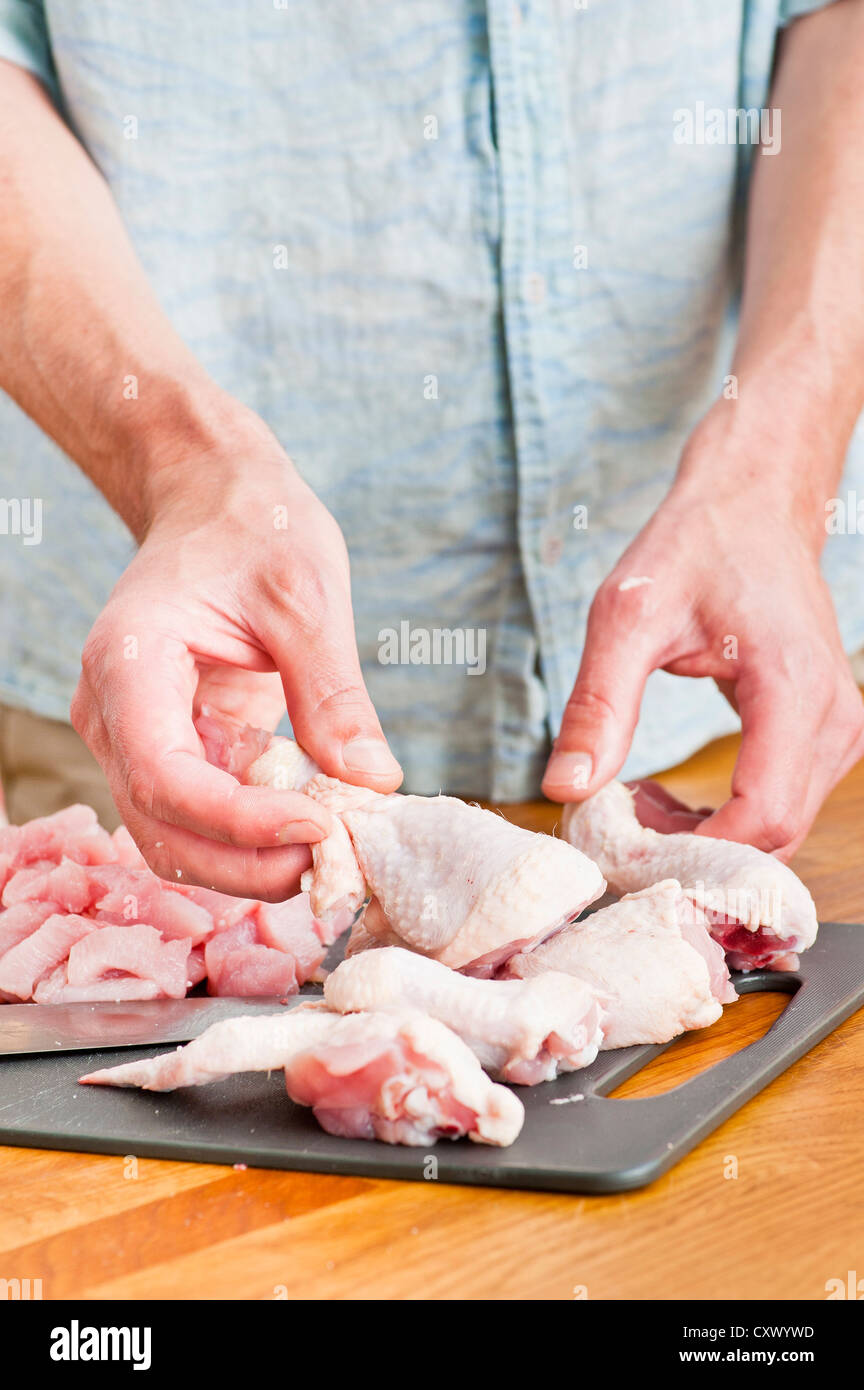 Man handling pieces of uncooked chicken in a kitchen Stock Photo