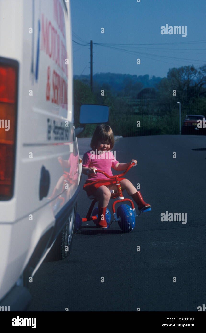 toddler on trike emerging onto road from the front of a van Stock Photo