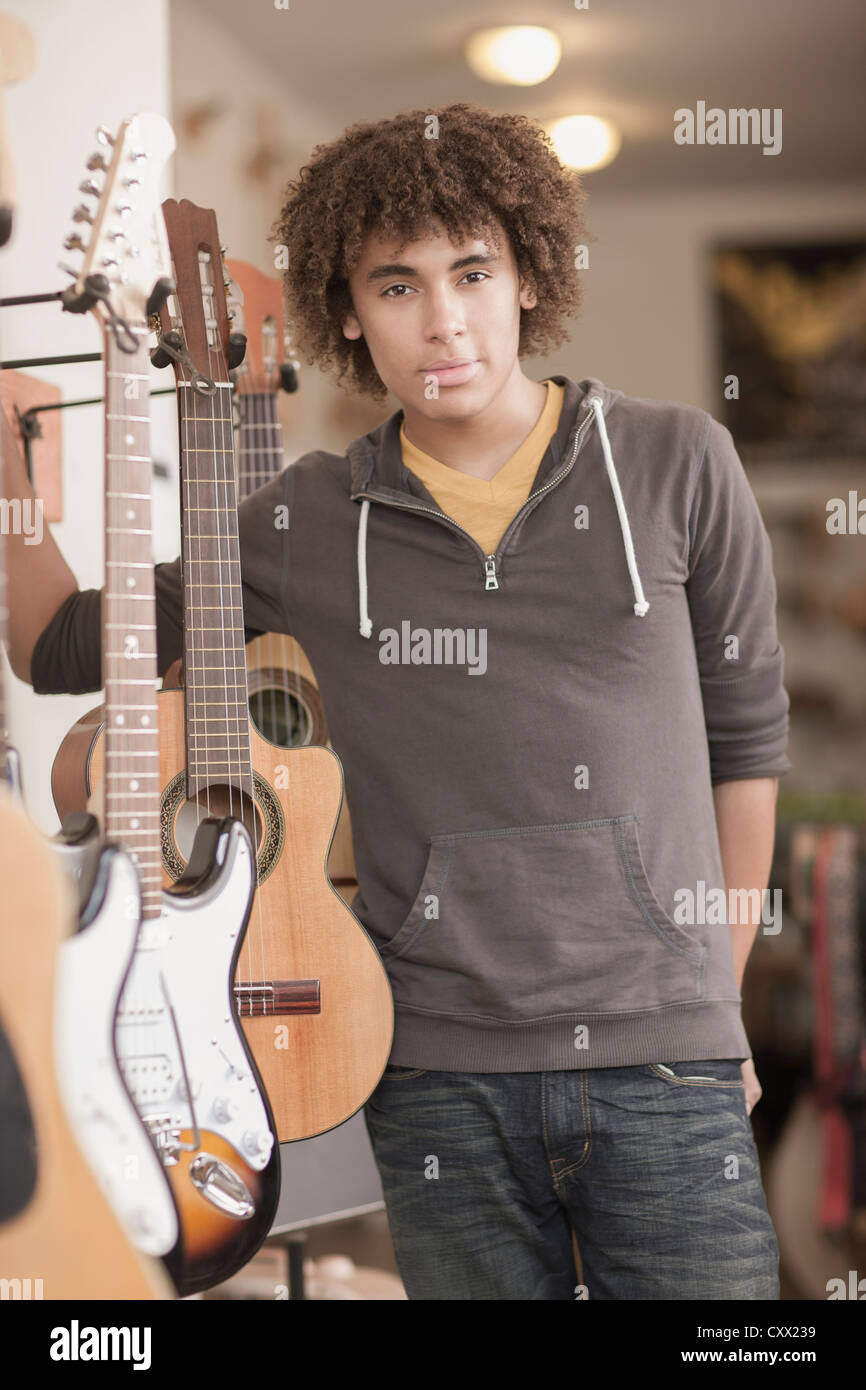 Mixed race teenager standing with guitars in music store Stock Photo