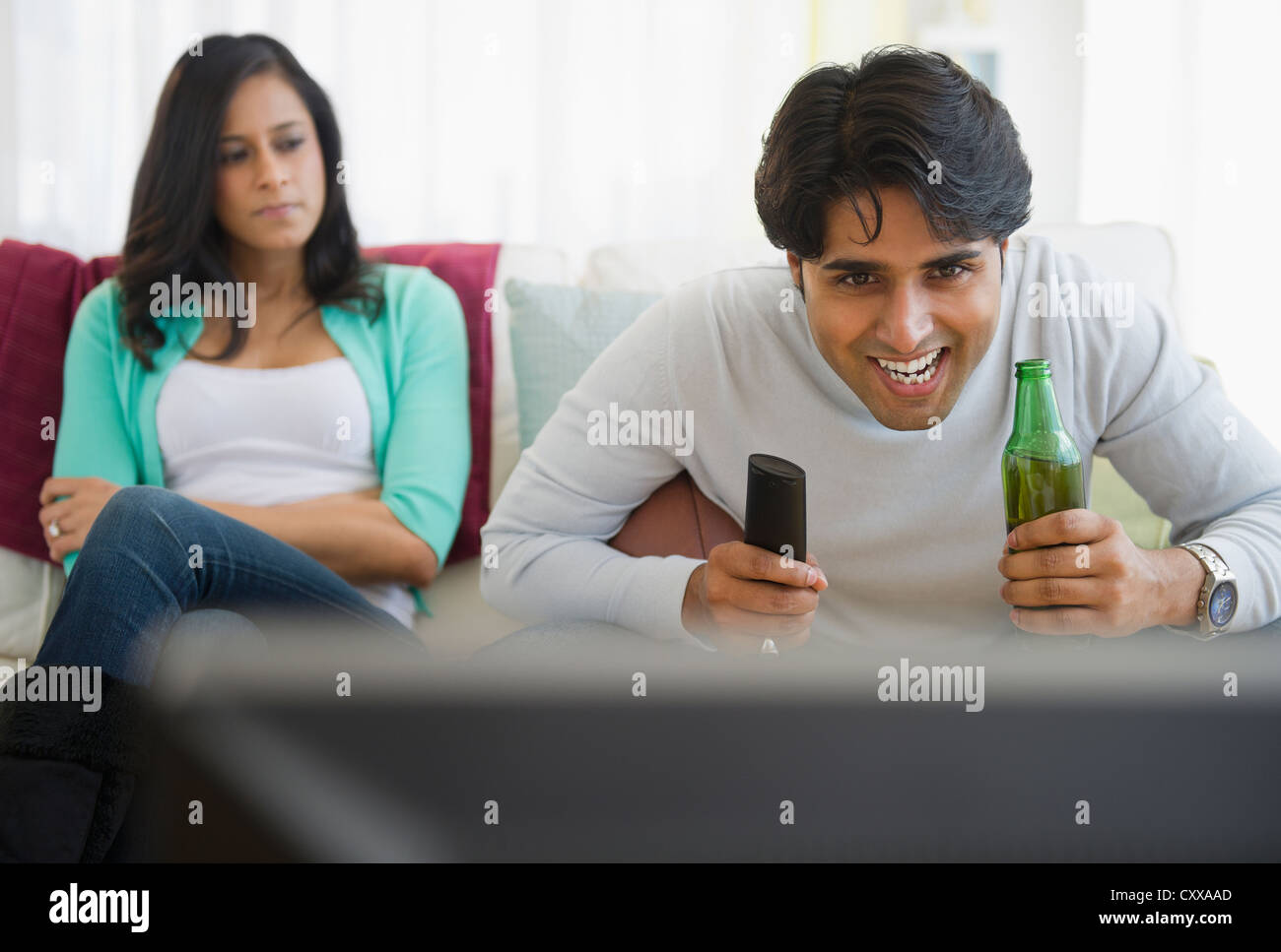 Angry girlfriend watching husband enjoy television Stock Photo