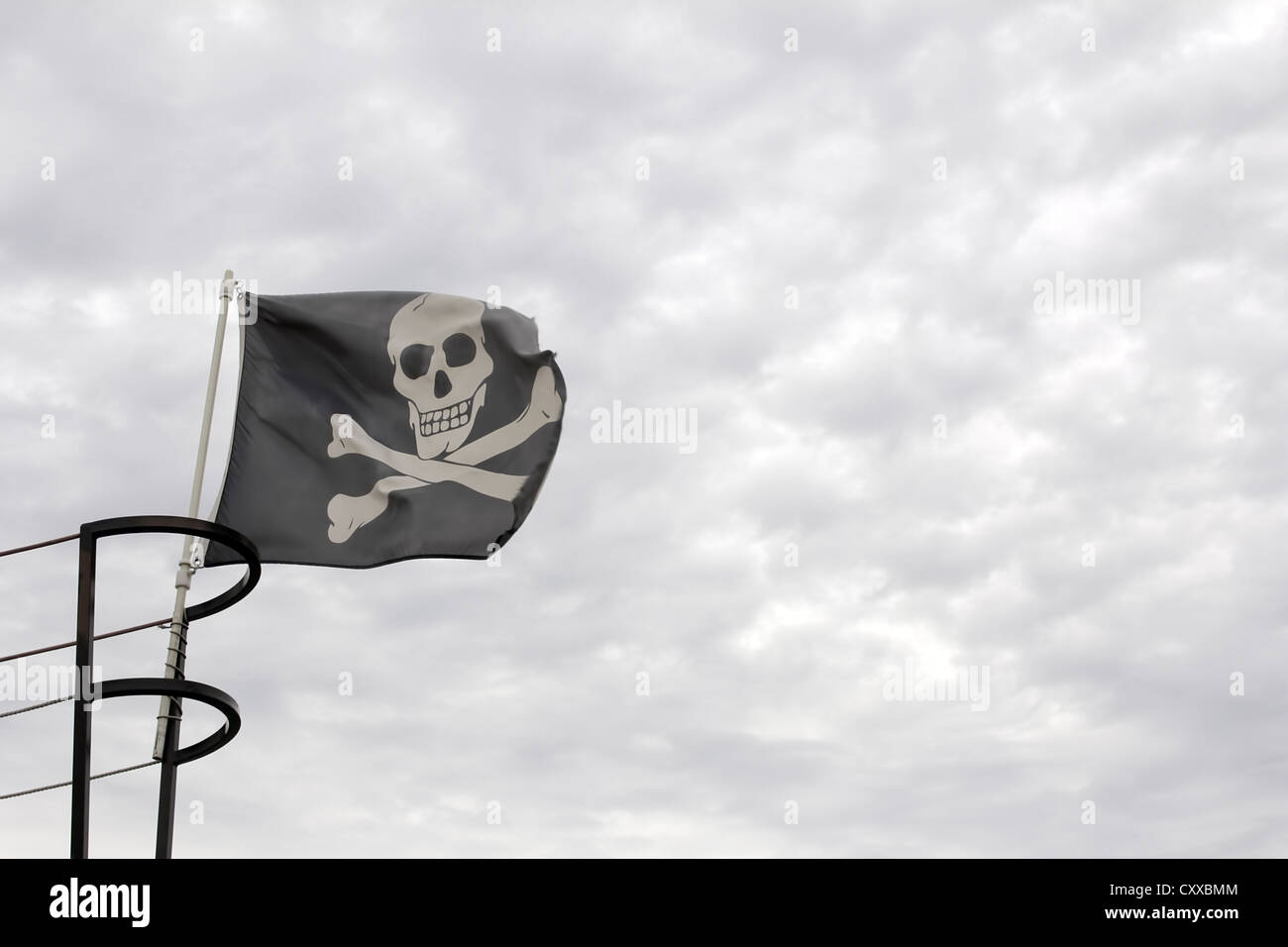Pirate Ship Jolly Roger Skull with Crossbones Flag against Cloudy Sky Background Stock Photo