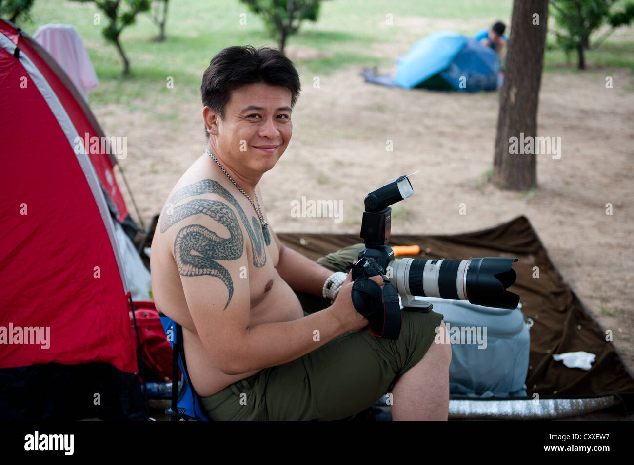 Chaoyang Park, Beijing. Amateur photographer with snake tattoo sitting in front of his - rented for a day - tent. Stock Photo