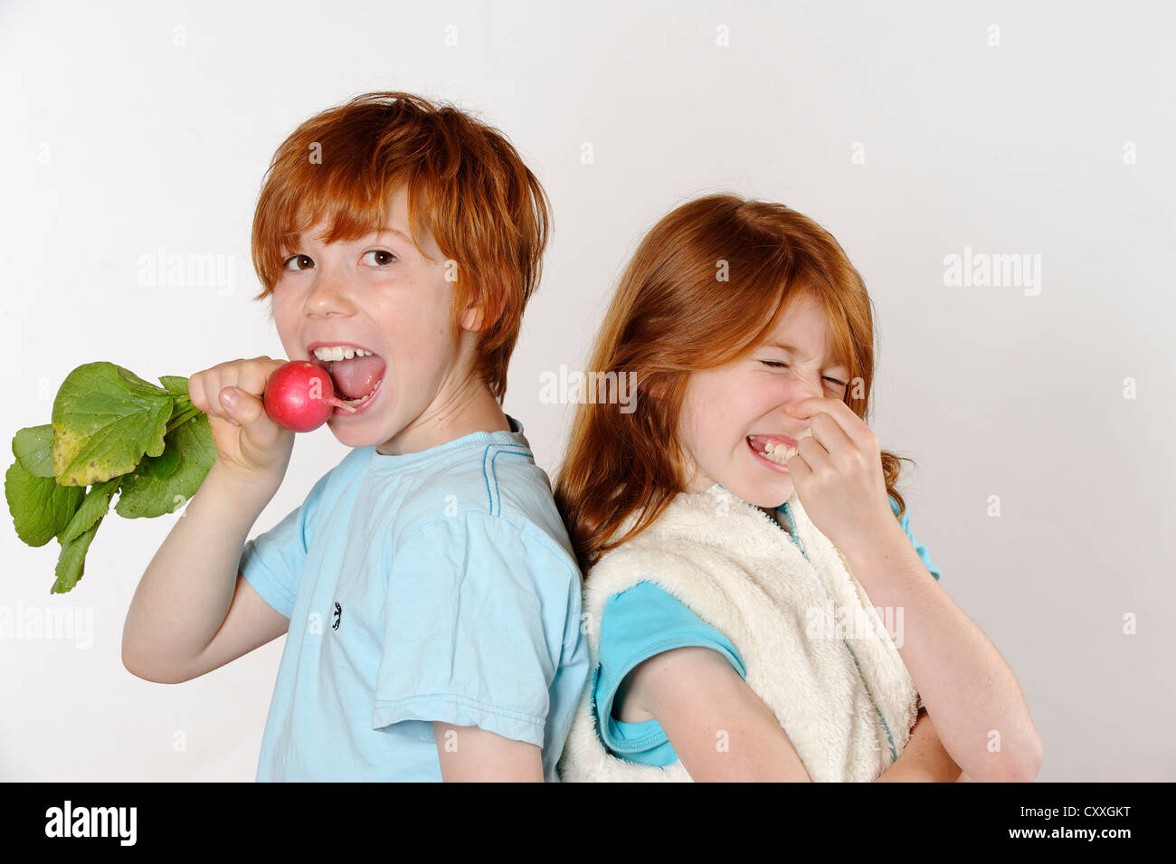 Boy eating radishes, girl rejecting raw food or vegetables Stock Photo