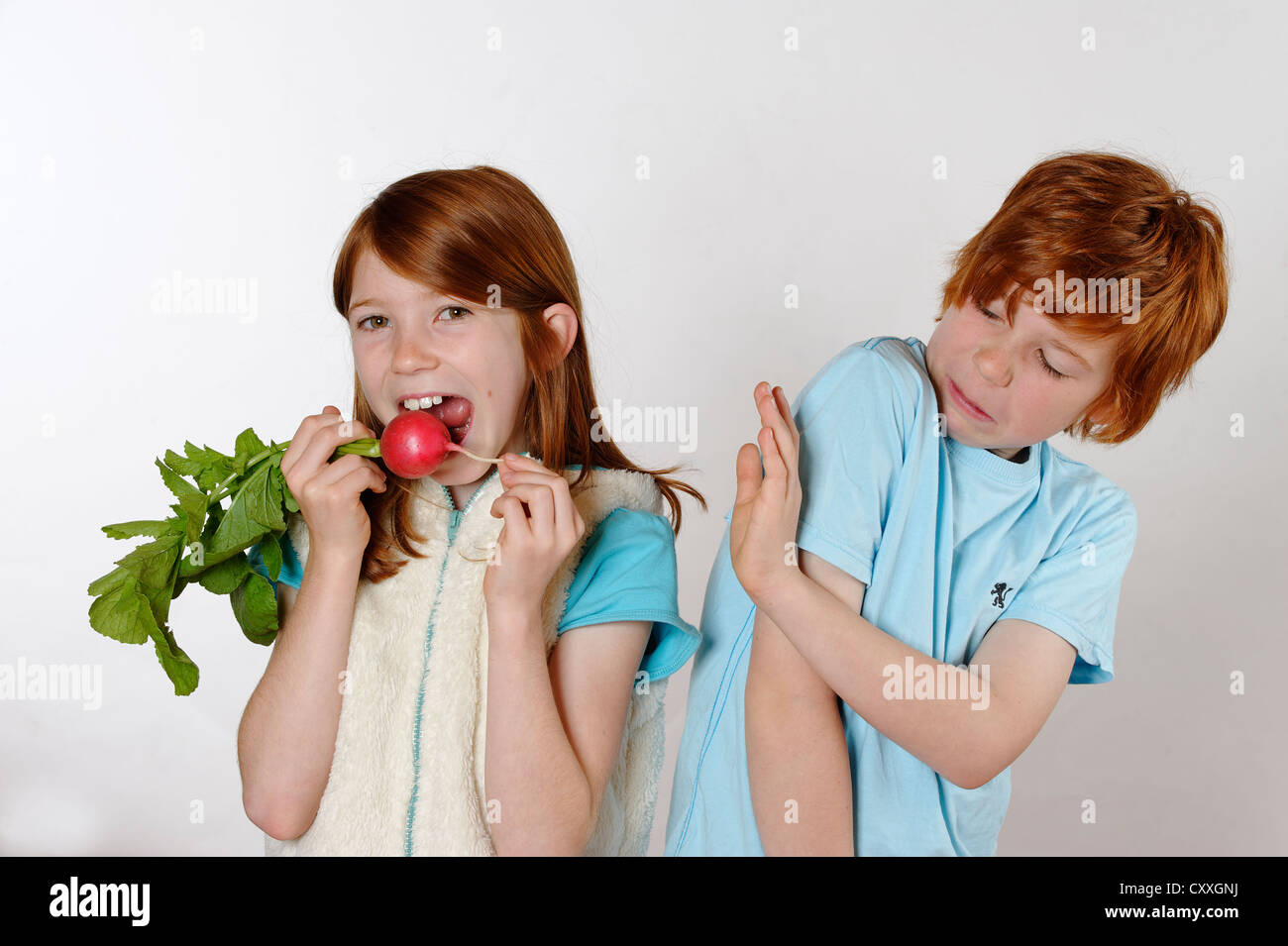 Girl eating radishes, boy rejecting raw food or vegetables Stock Photo