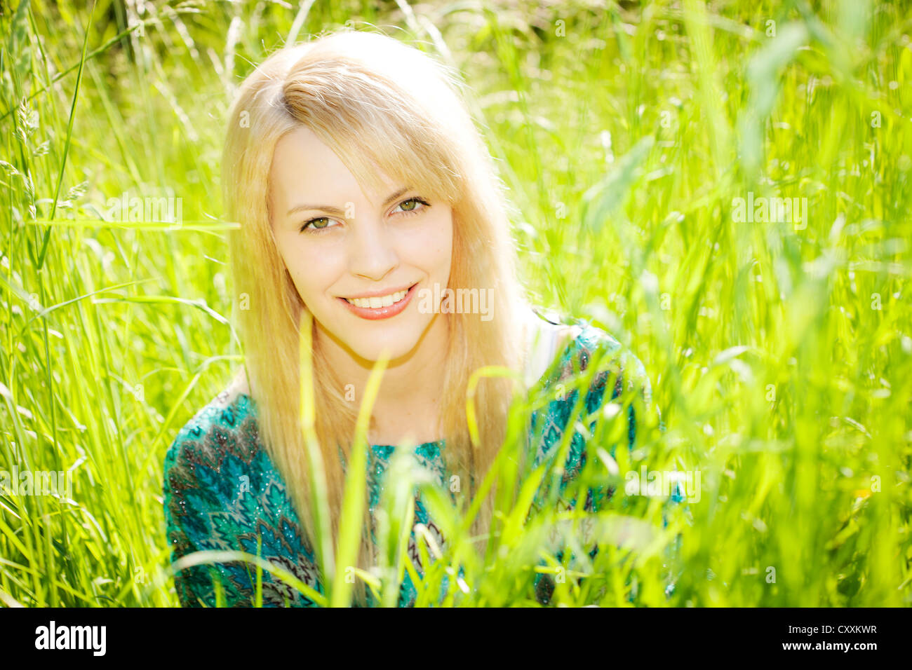 Smiling young woman sitting in tall grass Stock Photo - Alamy