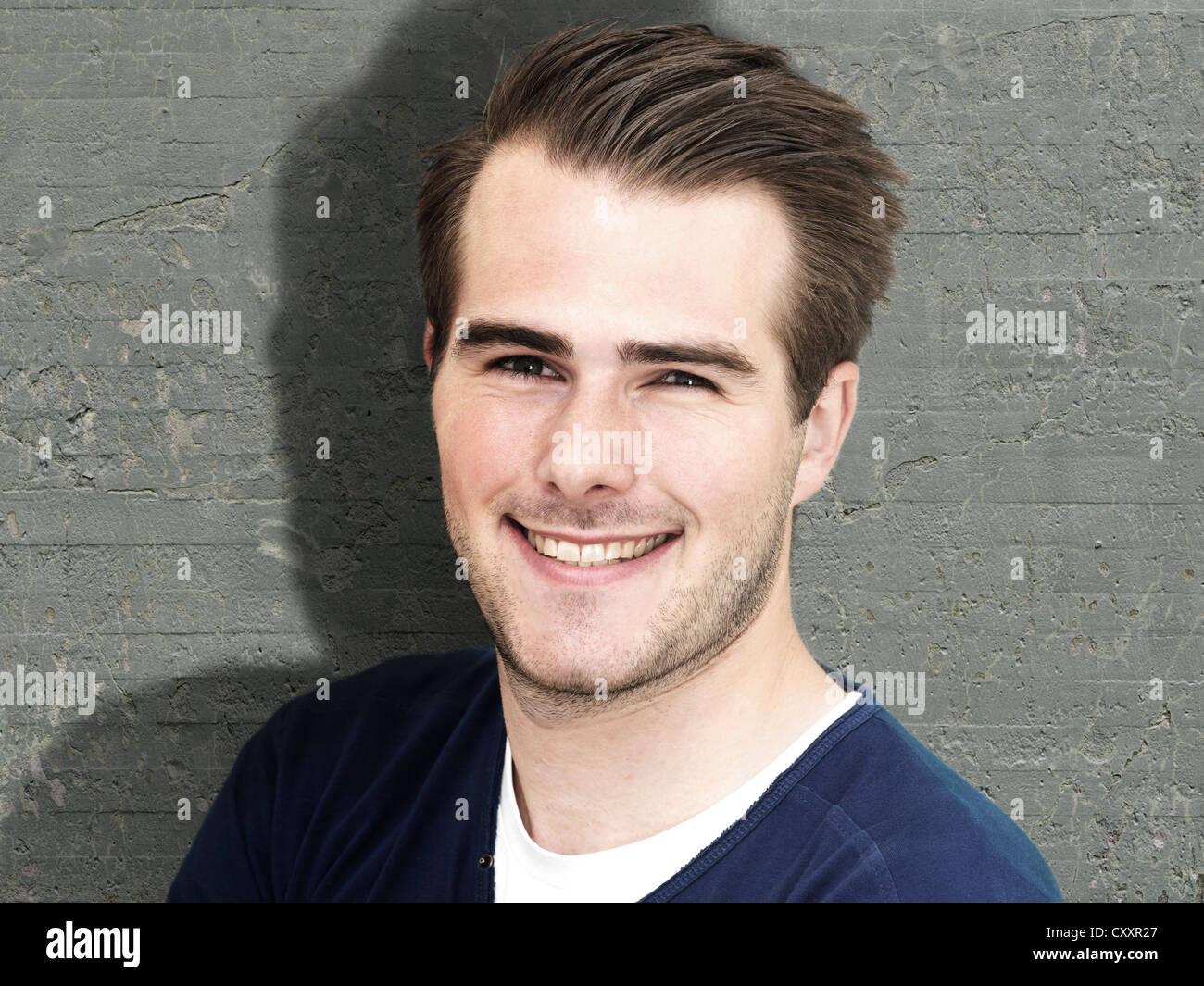 Smiling young man standing in front of a wall, portrait Stock Photo - Alamy