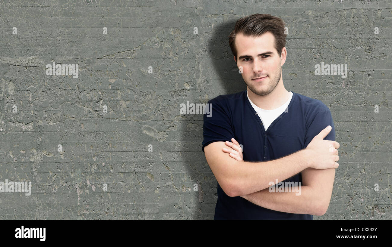 Young man leaning against a wall with his arms folded Stock Photo - Alamy