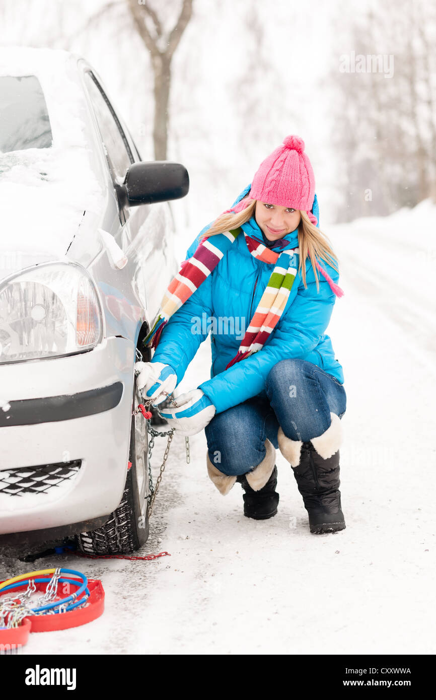Woman putting winter tire chains on car wheel snow breakdown Stock
