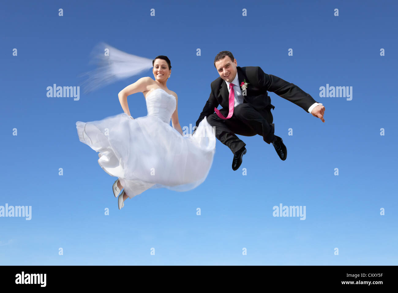 Bride and groom, bridal couple jumping into the air, against a blue sky ...