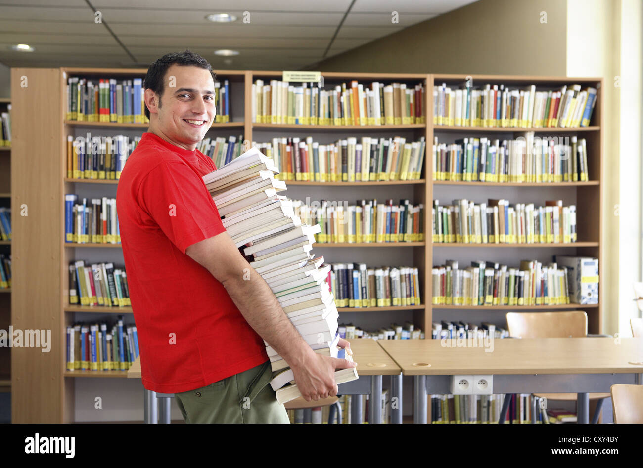 Smiling student carrying a huge pile of books, university library Stock ...