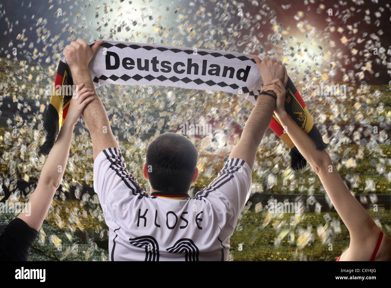 Football fan holding up a German supporters scarf, seen from behind, with confetti in a football stadium Stock Photo
