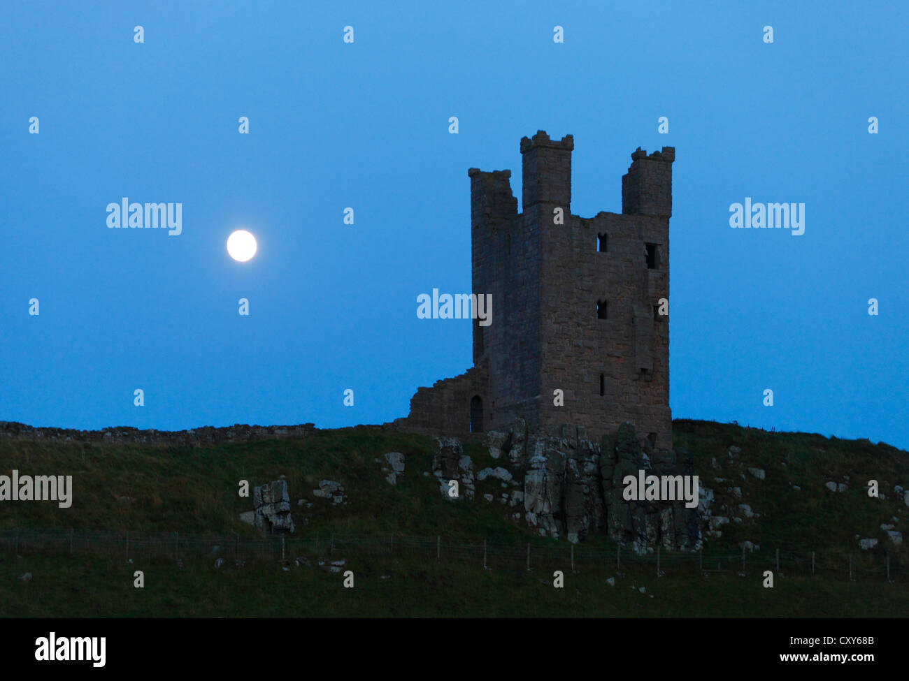 Dunstanburgh Castle, Northumberland, England at dusk with the moon rising behind. Stock Photo