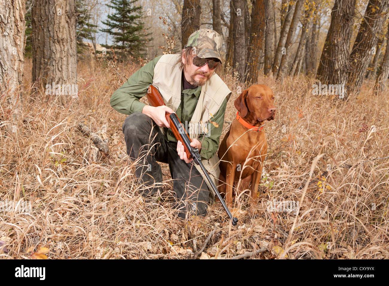 hunter kneeling beside his dog in the forest holding a gun ready for action Stock Photo
