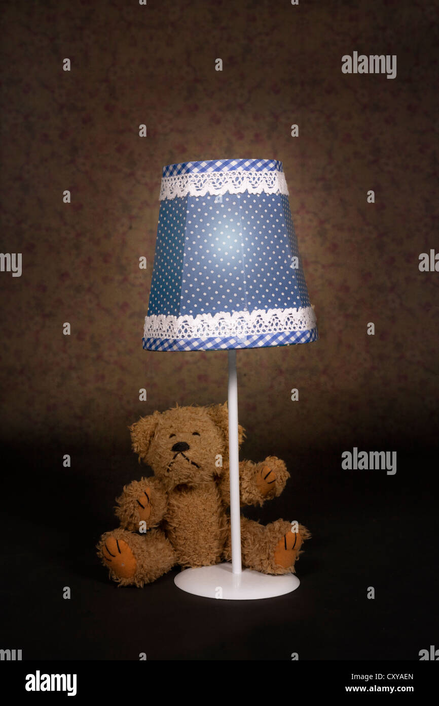 a teddy bear is sitting under an old vintage lamp Stock Photo