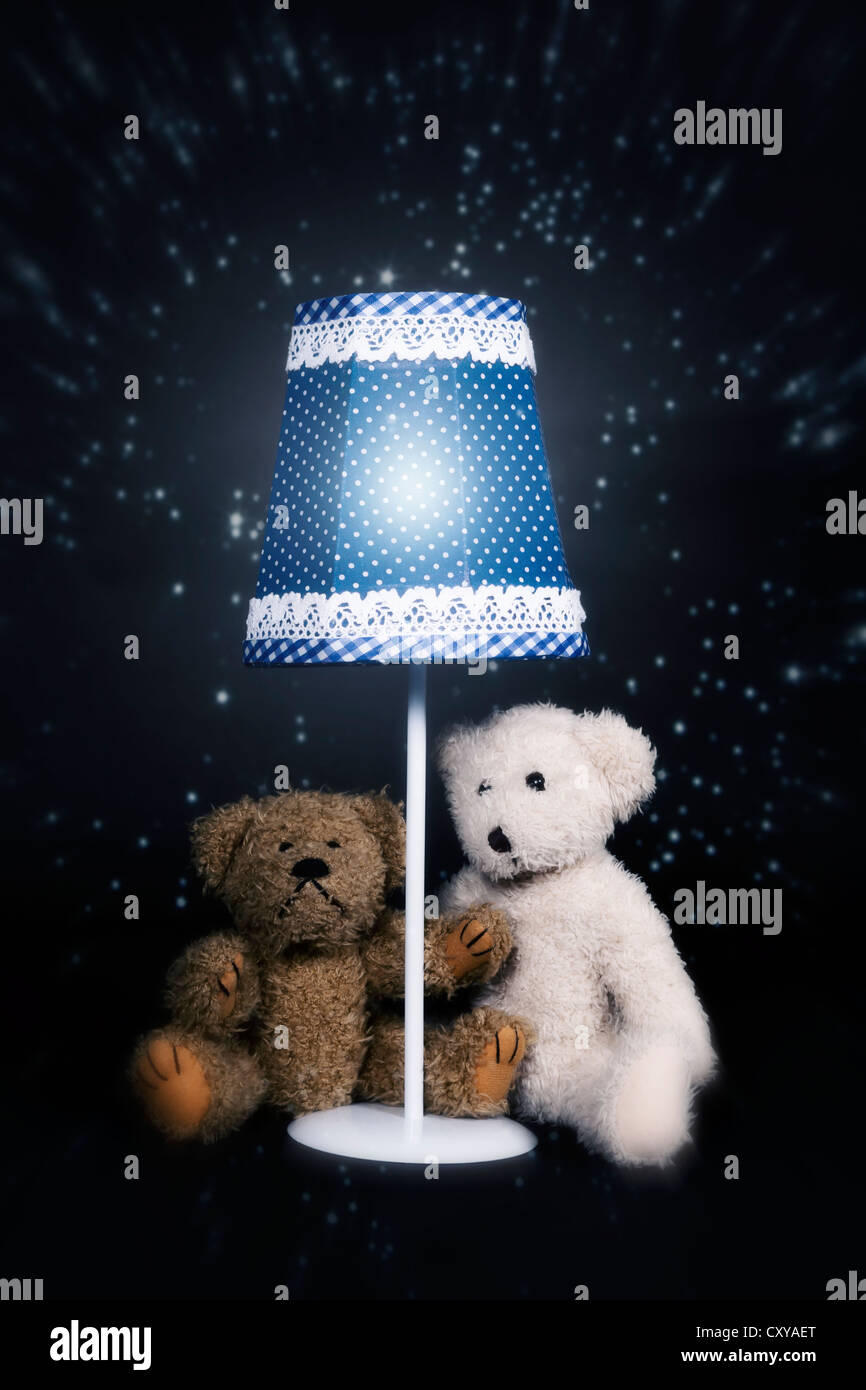 two teddy bears are sitting under an old vintage lamp Stock Photo