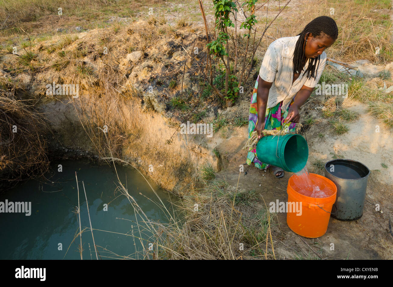 Woman taking water from a shallow groundwater open well. Kabwe. Zambia Stock Photo