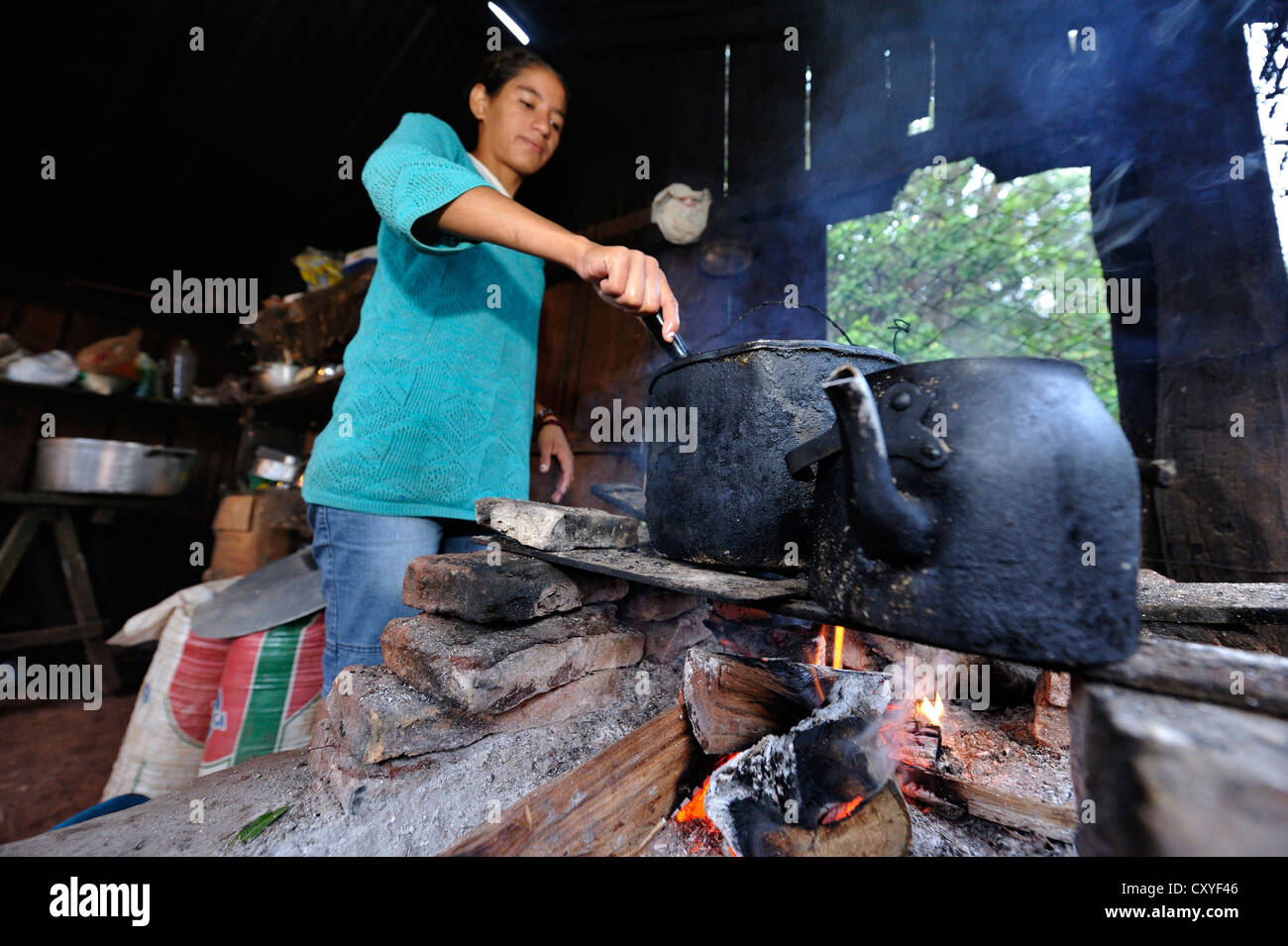 Young woman cooking over an open fire in the simple kitchen of farm workers, Comunidad Arroyito, Departamento Concepcion Stock Photo