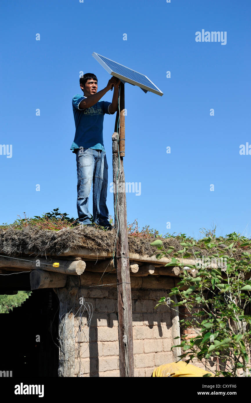 Young man mountain solar cells on the roof of a simple hut of a smallholder's farm, Gran Chaco, Santiago del Estero Province Stock Photo