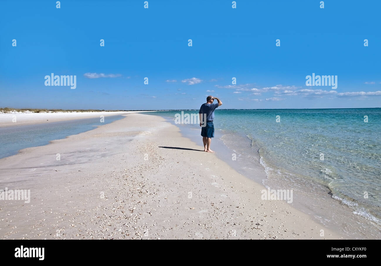A man standing on a long stretch of deserted beach looking out to sea. Stock Photo
