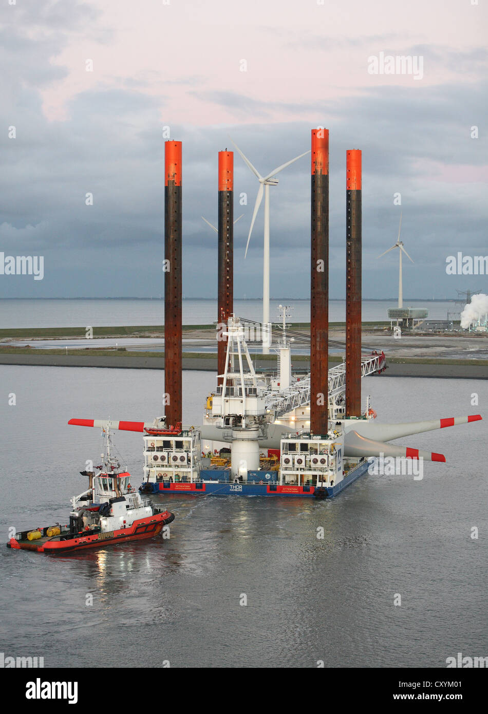 Ship used for the construction of offshore windfarms leaves Eemshaven carrying a wind turbine head, guided by tug boats. Stock Photo