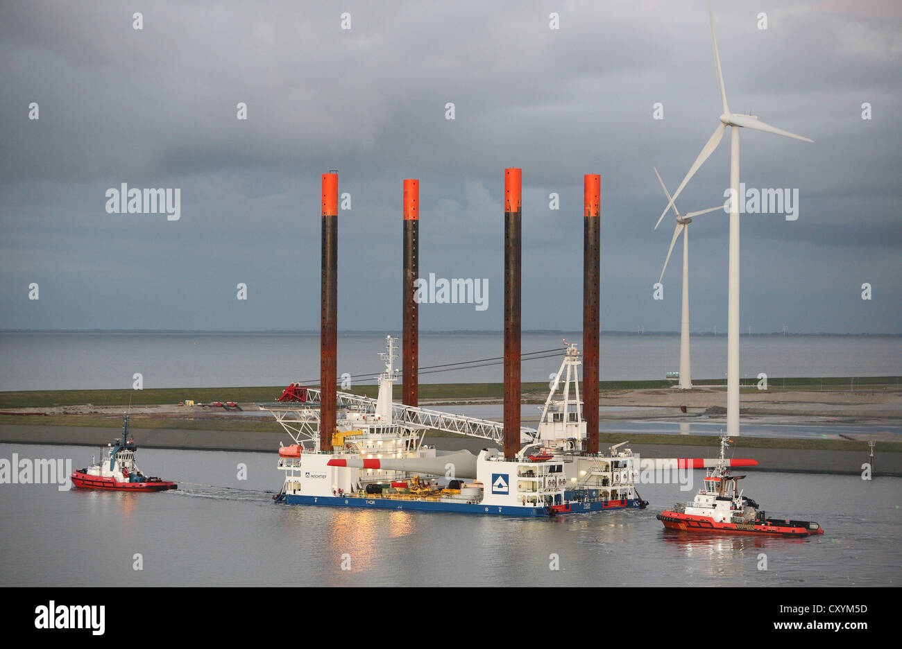 Ship used for the construction of offshore windfarms leaves Eemshaven carrying a wind turbine head, guided by tug boats. Stock Photo