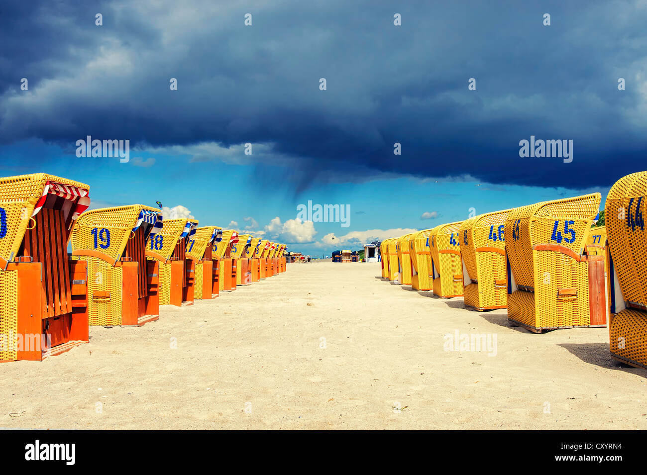 Two rows of yellow roofed wicker beach chairs in the sunshine, dark rain clouds at the back, Mecklenburg-Western Pomerania Stock Photo