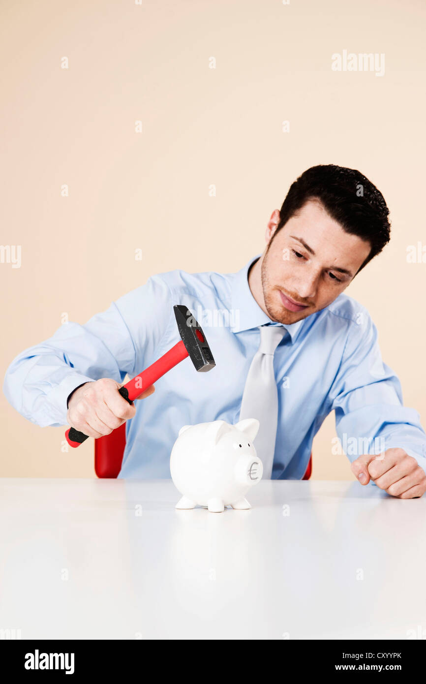 Young man about to hit a piggy bank with a hammer Stock Photo - Alamy