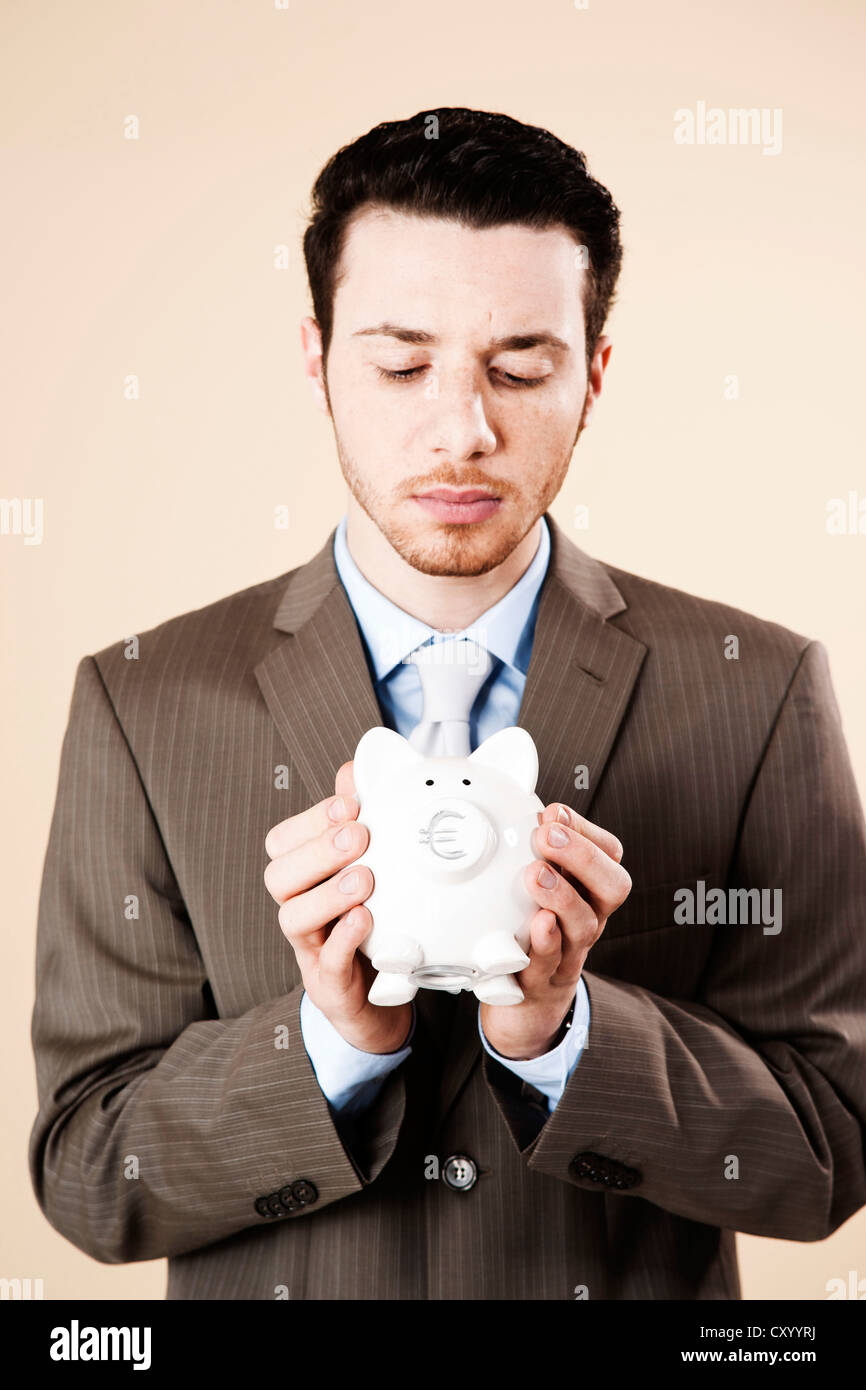 Young businessman with a concerned expression holding a piggy bank in