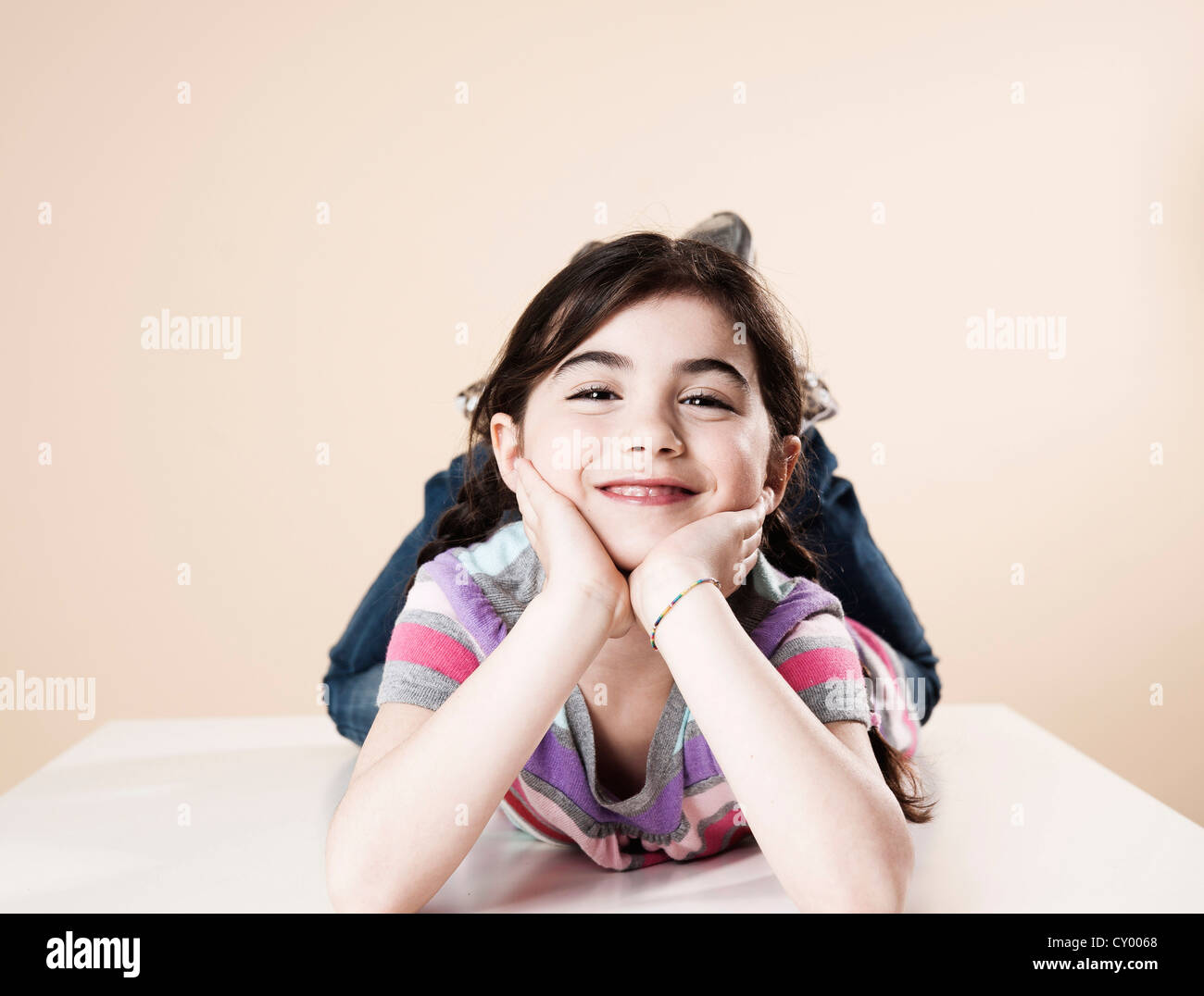 Smiling girl lying on her stomach with her head resting in her hands