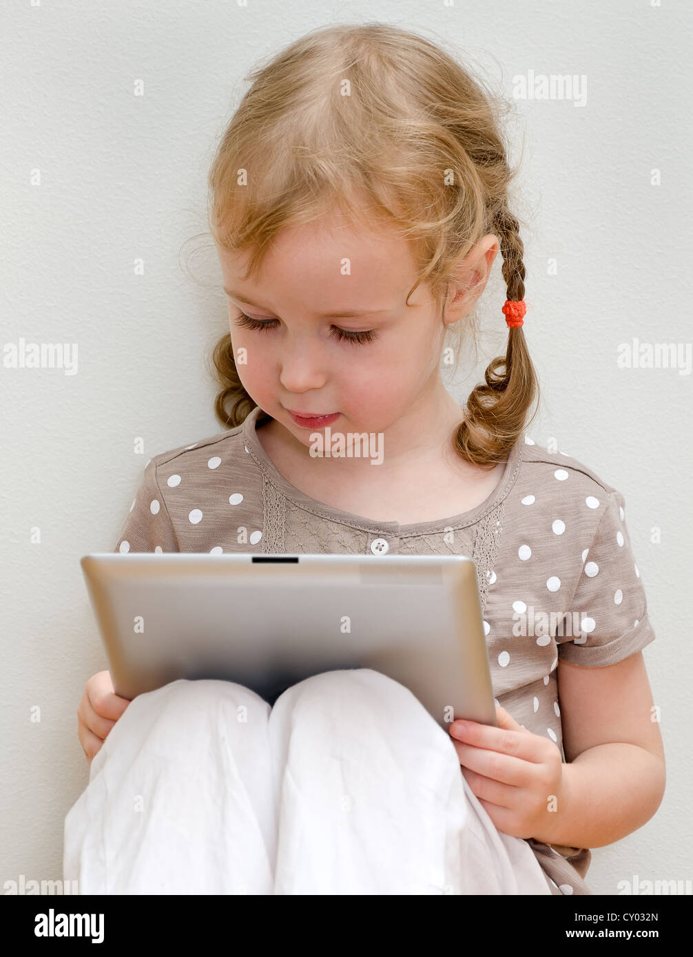 Cute little girl sitting against the wall and using tablet computer Stock Photo