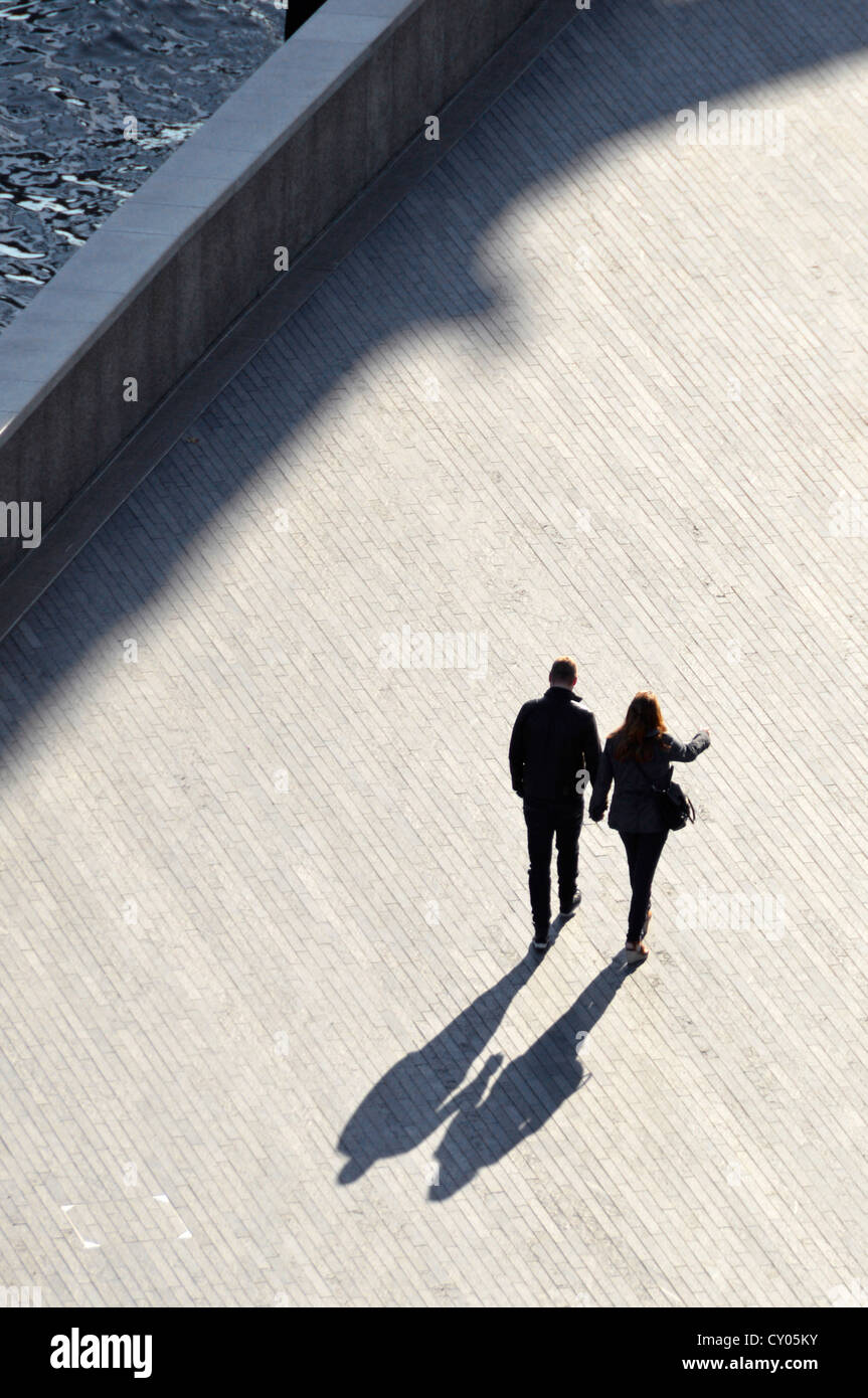 Aerial view silhouette couple walking hand in hand beside River Thames along riverside walk way possible book cover image Southwark London England UK Stock Photo