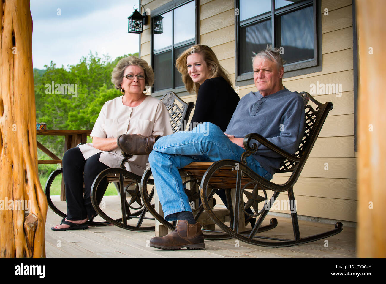 Family portrait of three mature people, parents and 35 years old daughter on the front porch of their house Stock Photo