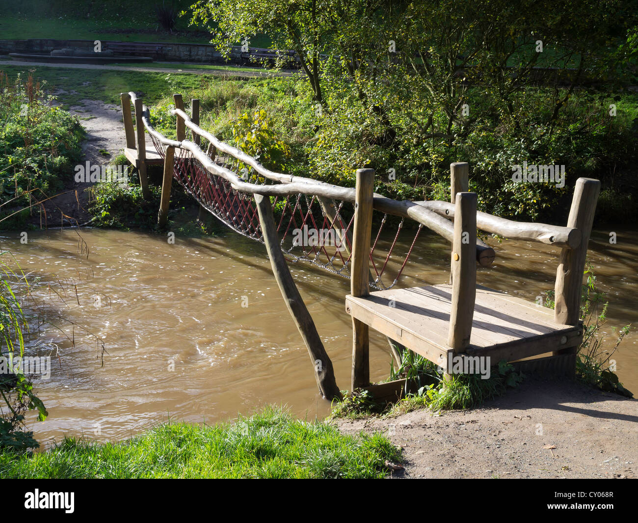A foot bridge across a stream with the footway being a single suspended chain for amusement of children Stock Photo