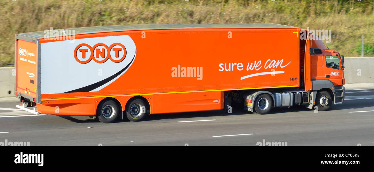 Side view TNT Express freight delivery business hgv supply chain lorry truck & articulated trailer driving along M5 motorway road Essex England UK Stock Photo