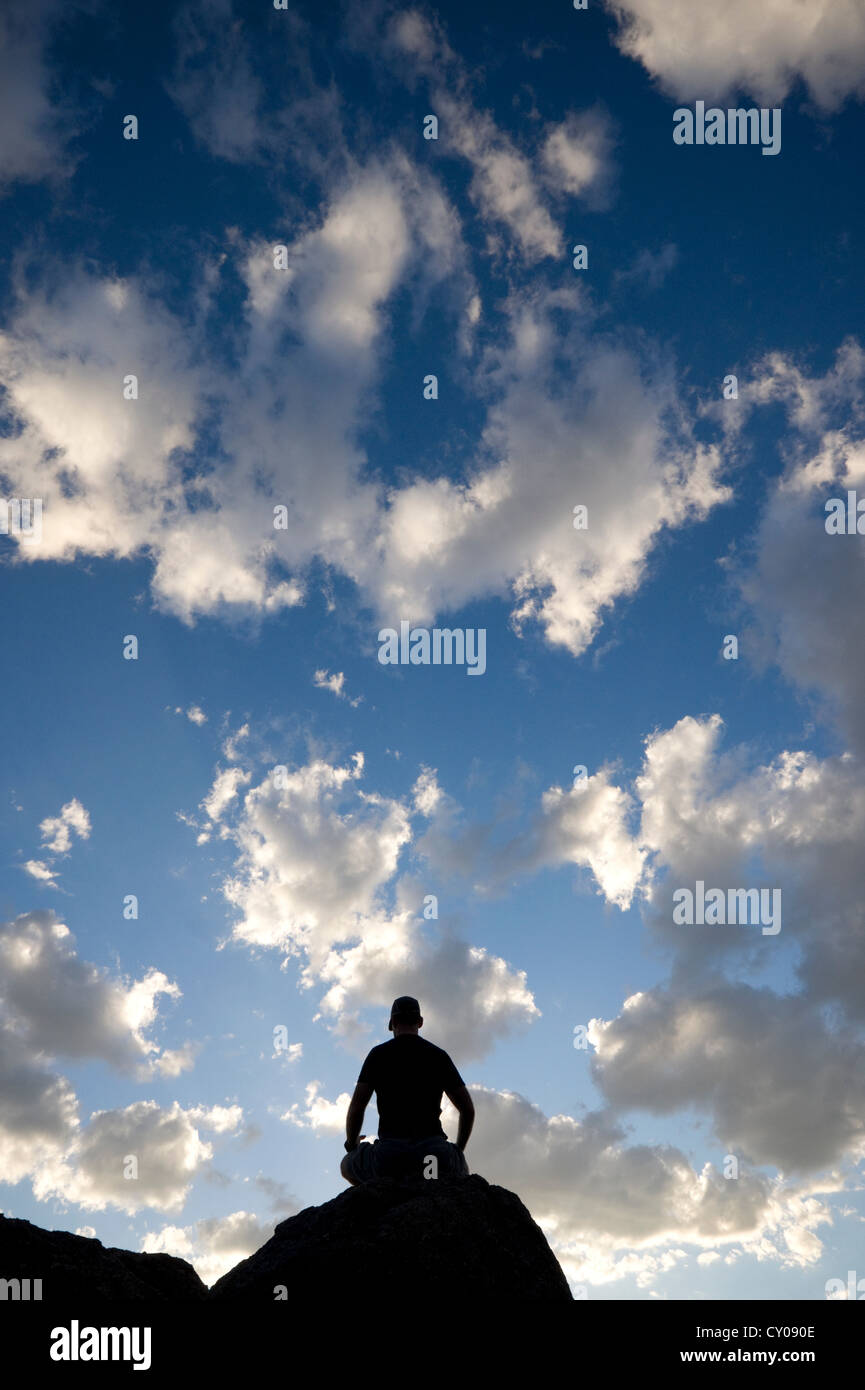 Silhouette of male figure sitting on rock in meditation Stock Photo