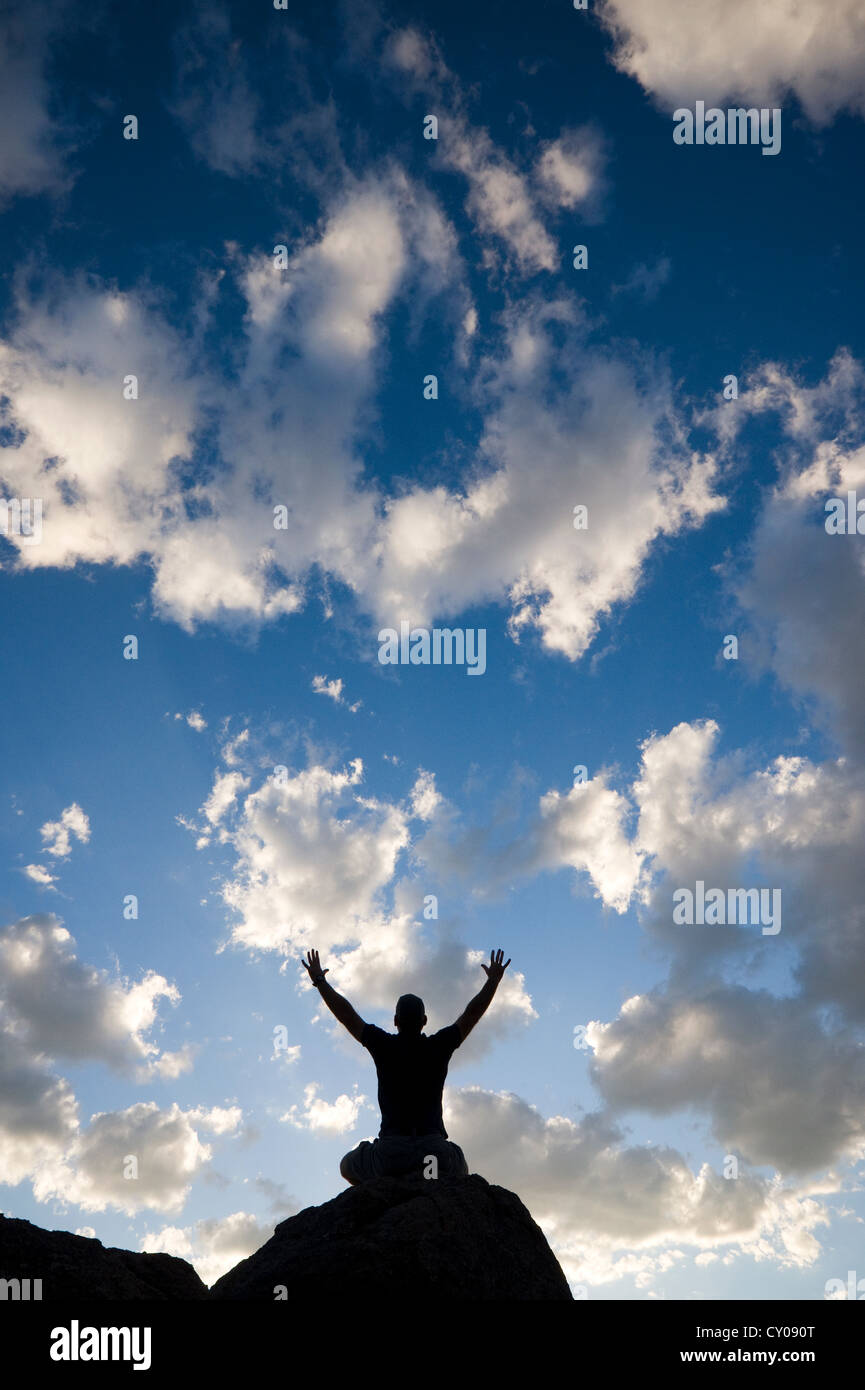 Silhouette of male figure sitting on rock with arms raised Stock Photo