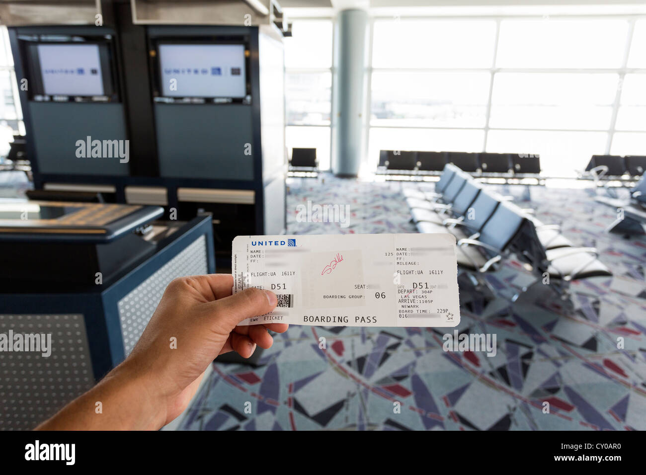 Hand holding a boarding pass. Airport gate in the background. Stock Photo