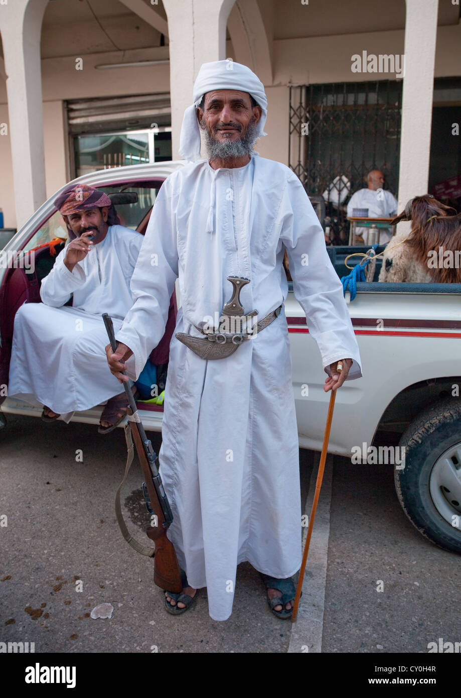 Old Man Wearing A Khanjar And Holding A Gun In The Right Hand While A Stick In The Left Hand, Ibra, Oman Stock Photo