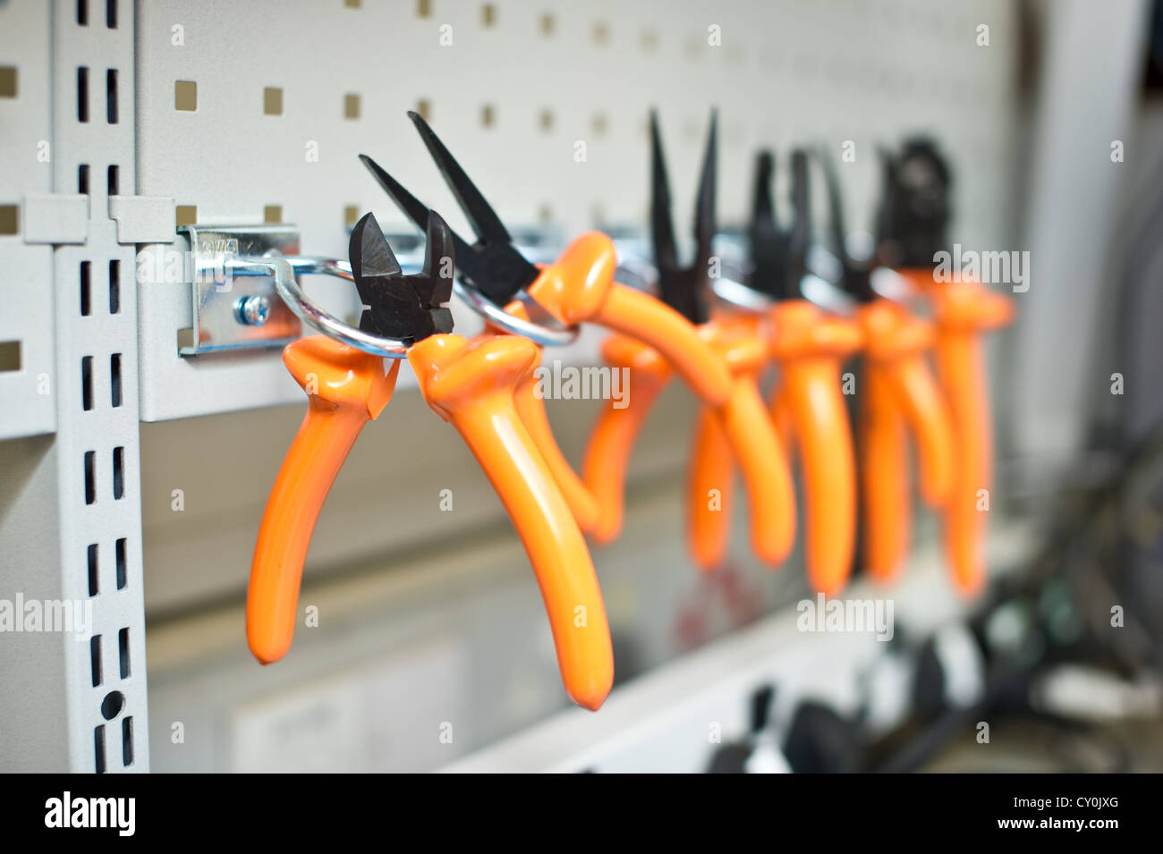 A series of insulated orange pliers on a rack. Stock Photo