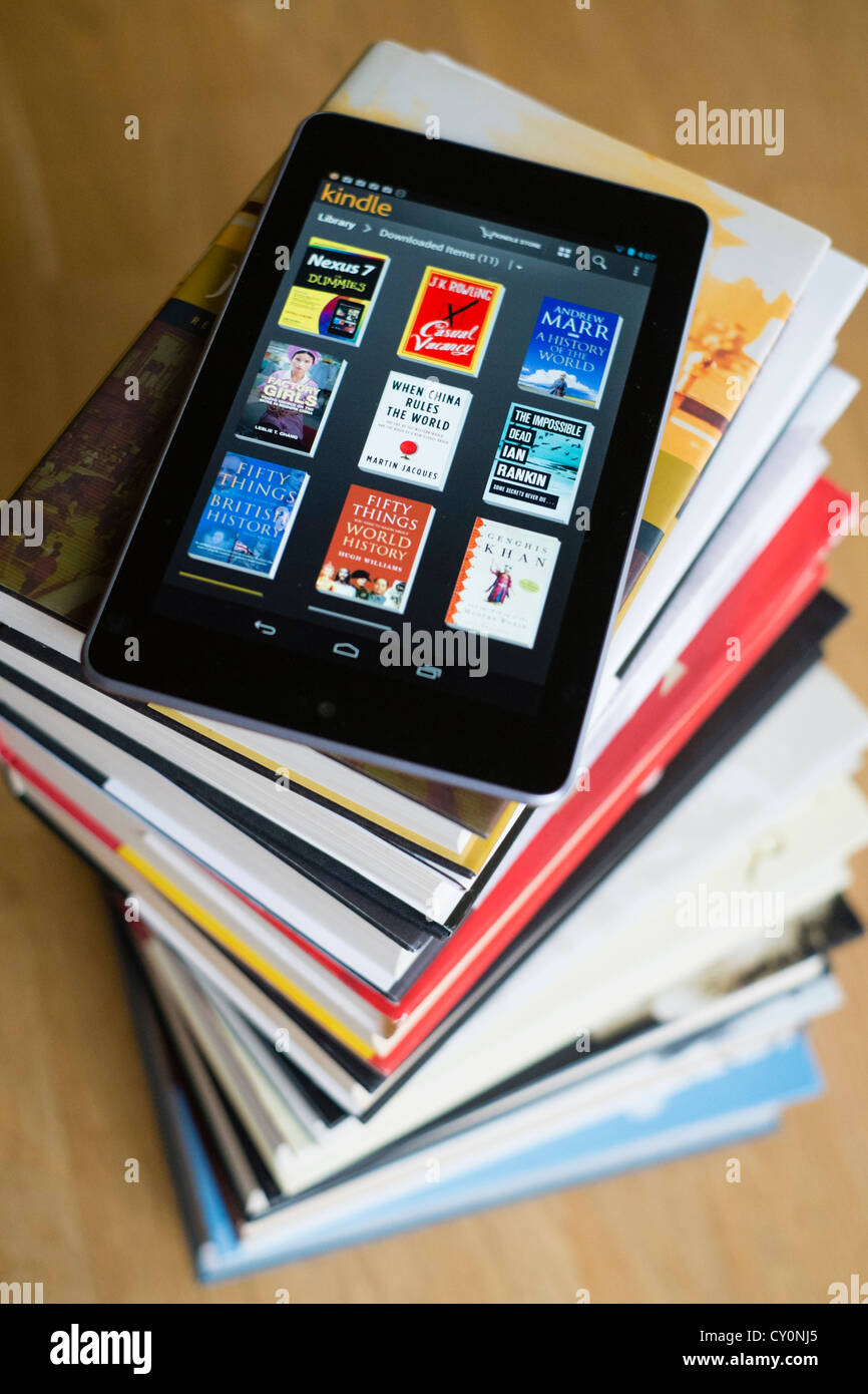 Google Nexus 7 tablet computer with kindle e-book library application and pile of traditional hardback paper books Stock Photo