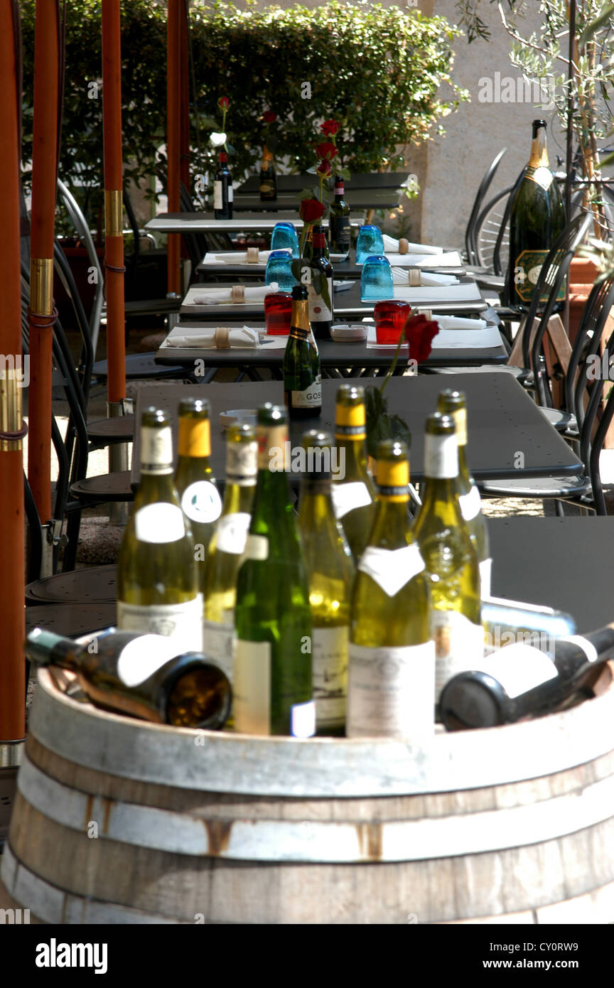 Empty wine bottles sitting on a barrel outside a restaurant with set tables in the background Stock Photo