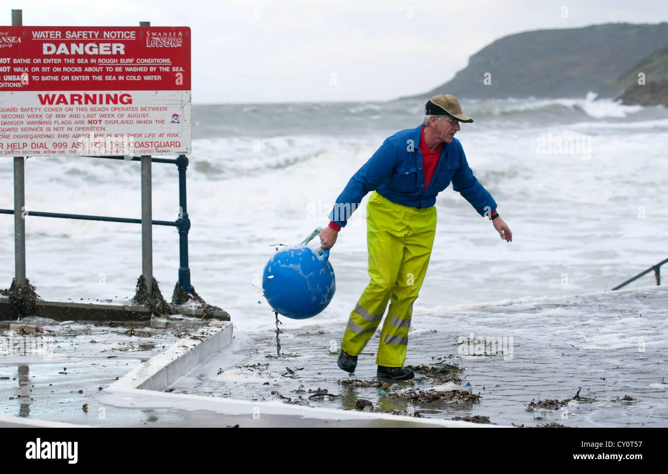 A Swansea Council workman retrieves a buoy from the debris washed up at high tide in the rough seas off Caswell Bay near Swansea Stock Photo