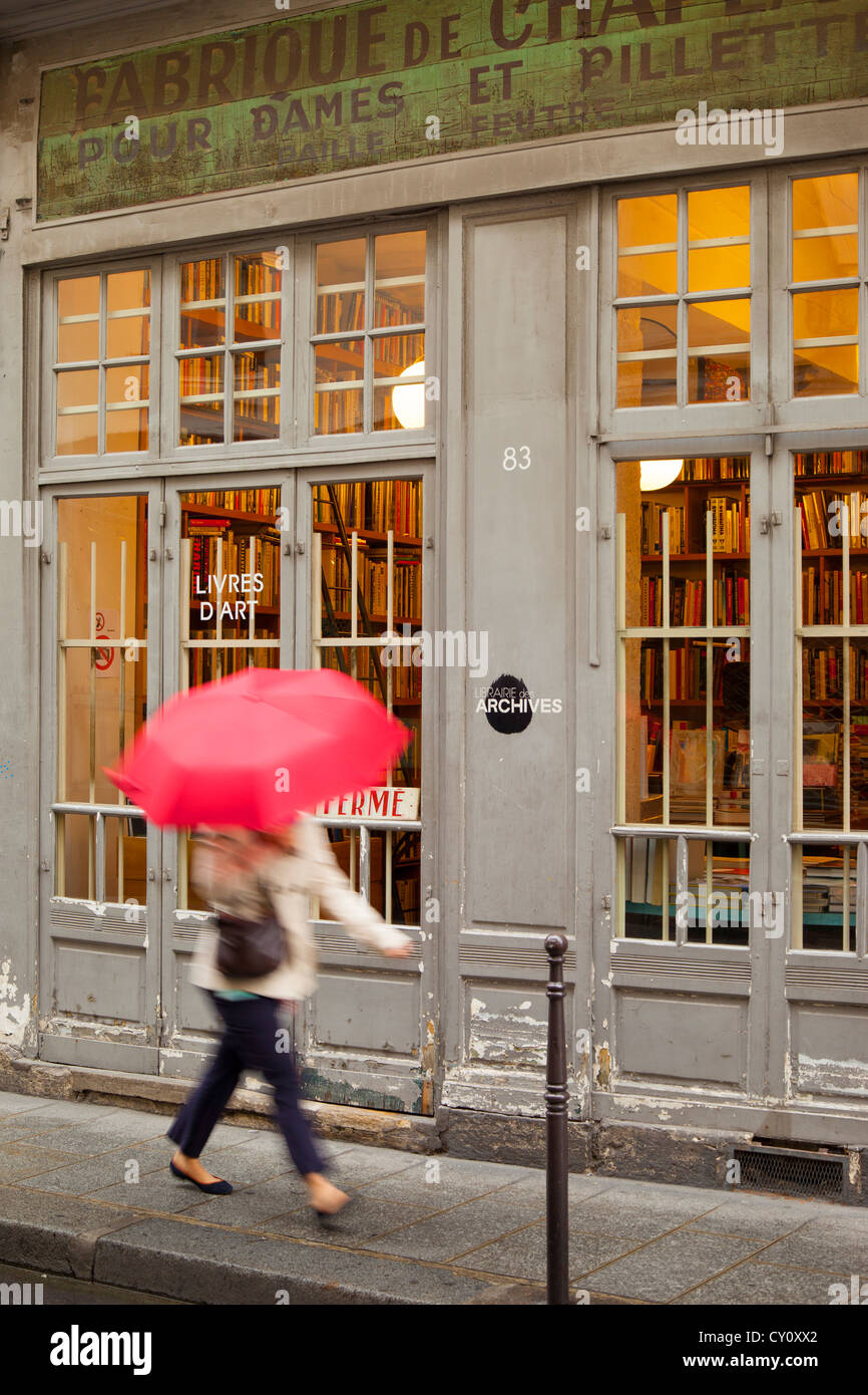 Woman with pink umbrella walks past a bookstore in historic Marais district, Paris France Stock Photo