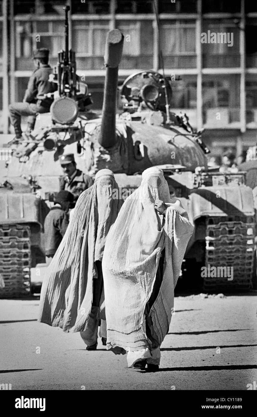 Afghan women wearing full body cover called a burqa walk past a Soviet T-62 tank guarding a street February 2, 1989 in Kabul, Afghanistan. Stock Photo