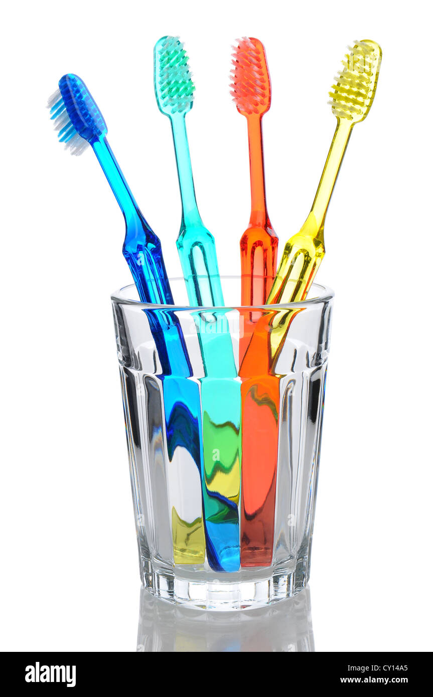 Four multi-colored-toothbrushes standing in a water glass. Vertical format over a white background with reflection. Stock Photo
