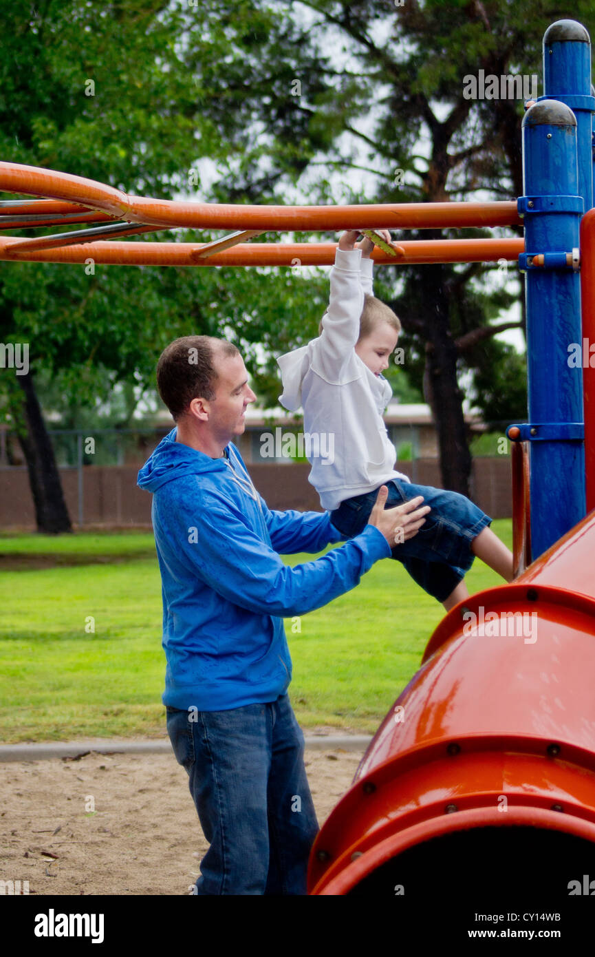 A dad provides support as his autistic son tries to hang from the monkey bars. Stock Photo