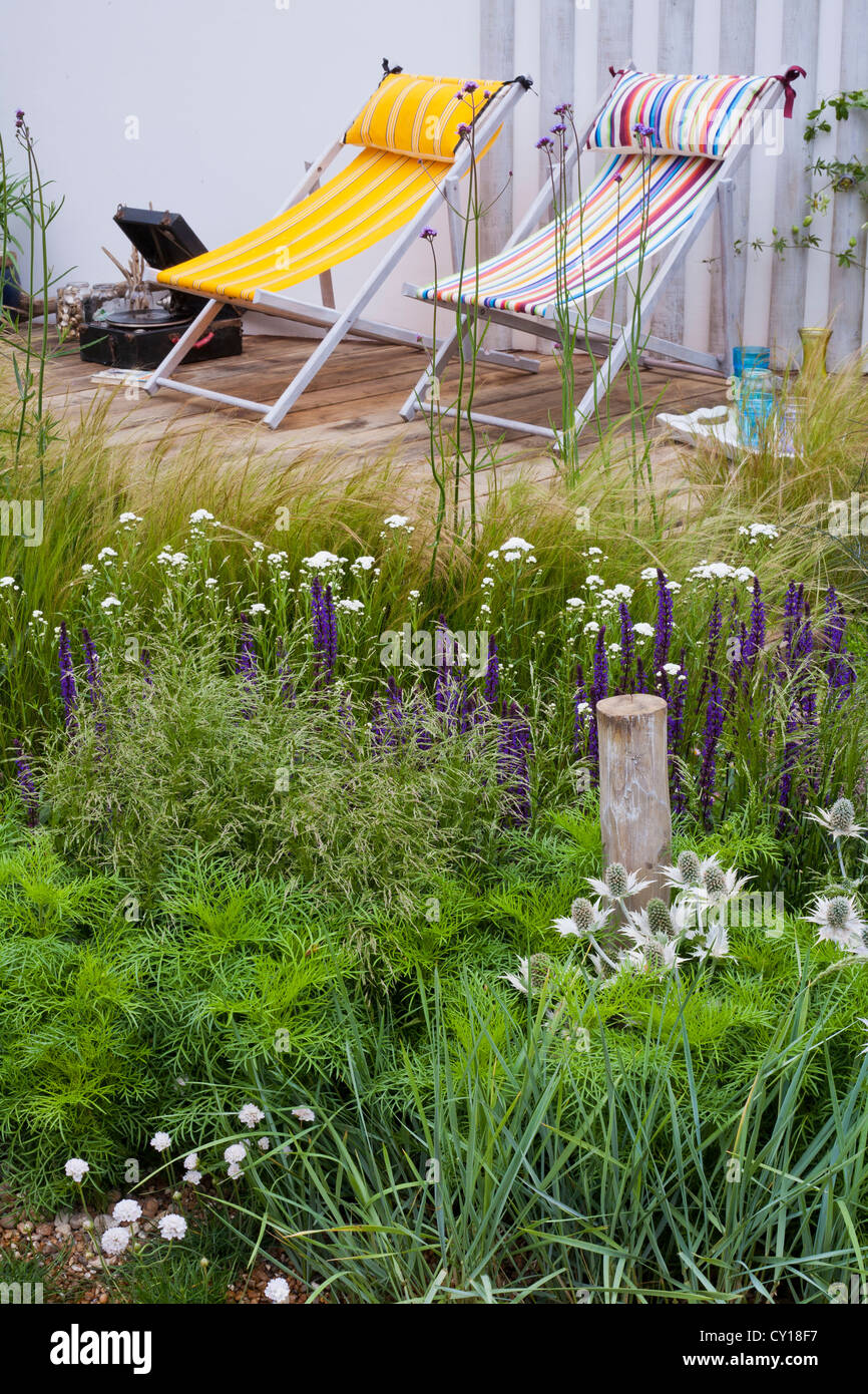 Extensive planting of grasses around timber decked patio area and above the curving back wall Stock Photo